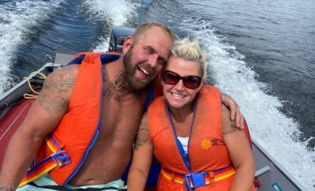 two people wearing lifejackets travelling in a boat on a lake 